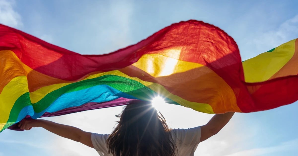 a woman holding a rainbow flag in front of a blue sky